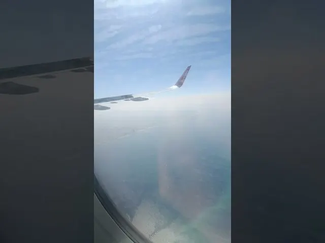 Aerial view from airplane window showing wing and clouds below