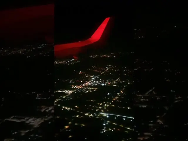 Red airplane wing glowing at night above city lights below
