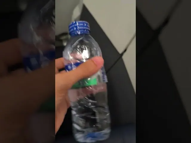 Hand holding plastic water bottle with blue cap on airplane