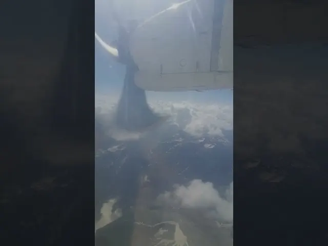 Aircraft wing and engine viewed from window above clouds mountains