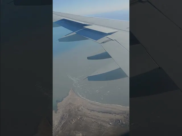 Aircraft wing with four blue engines flying over desert landscape