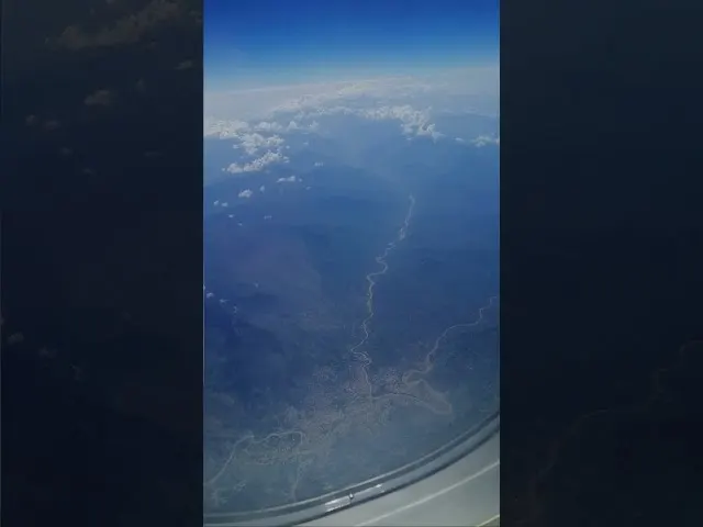 Aerial view of river winding through landscape below aircraft wing