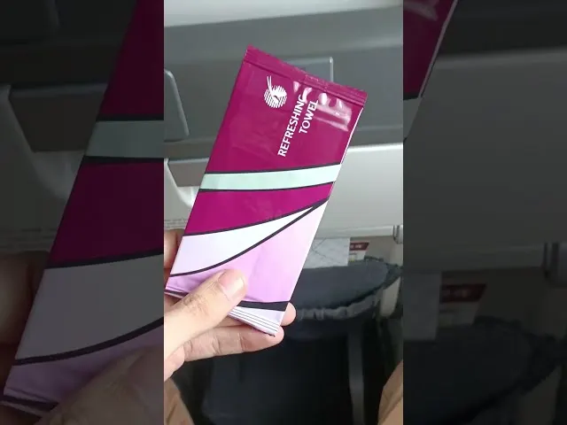 Hand holding Qatar Airways amenity kit with pink and magenta branding