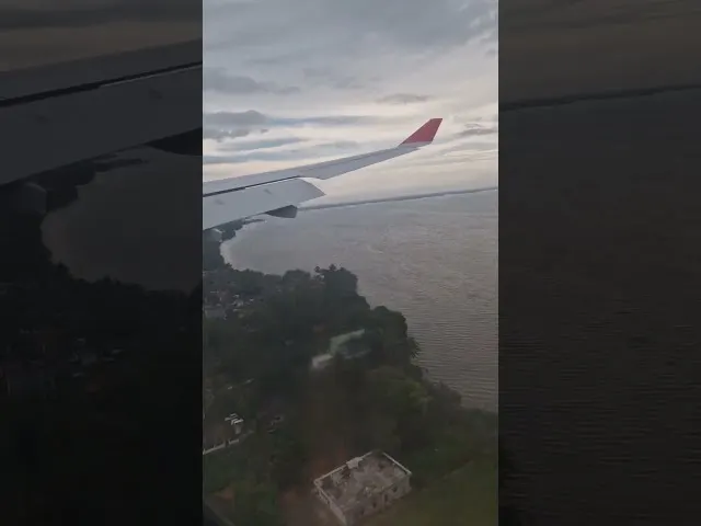 Aircraft wing with red winglet over coastal landscape and water