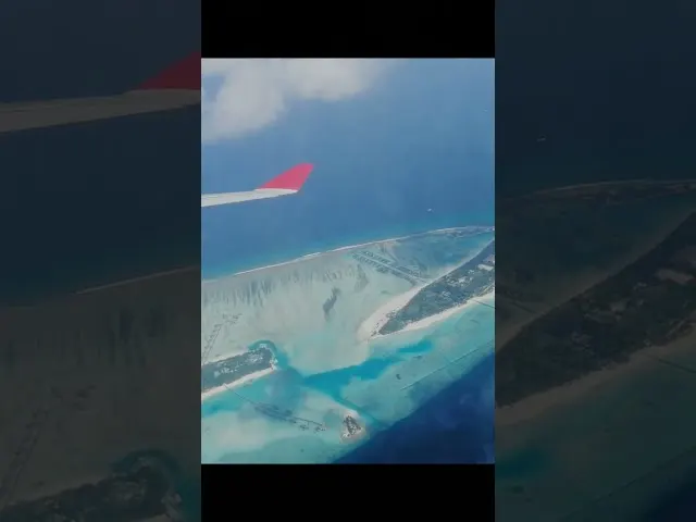 Airplane wing with pink winglet flying over tropical turquoise island waters